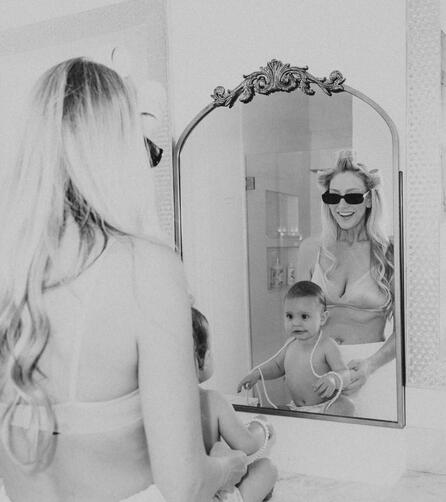 NOSTALGIA IN NOIR // Classic, grainy black-and-white portraits that transcend time. Black and white high-fashion editorial photograph of a mother with hair rollers holding her infant daughter in front of dramatic silk window drapes at a luxury film location.